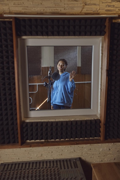 smiling-african-american-young-woman-singer-standing-near-microphone-inside-soundproof-room-recording-studio_386167-16562